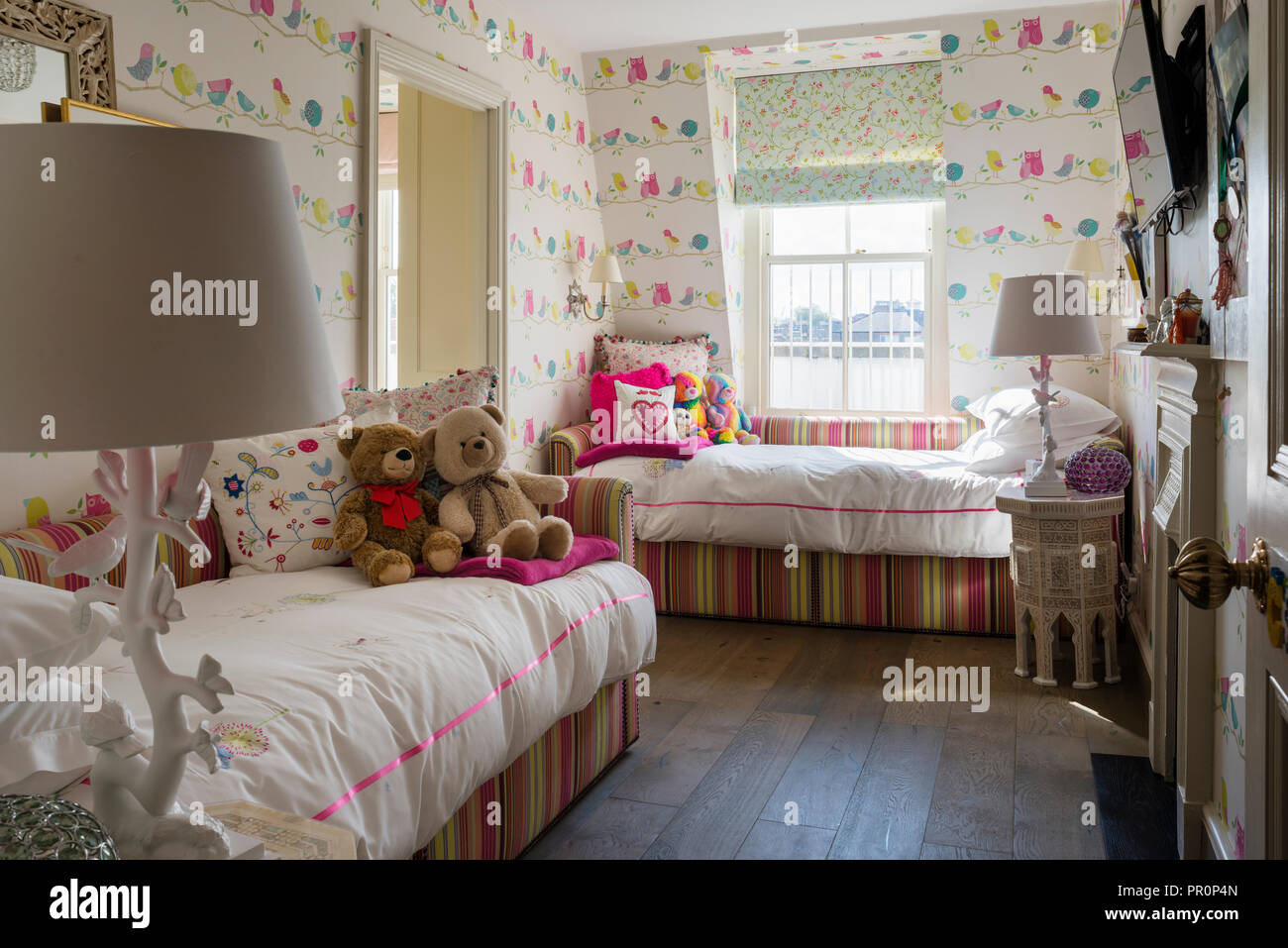 Striped daybeds with bird patterned wallpaper in girls room Stock Photo