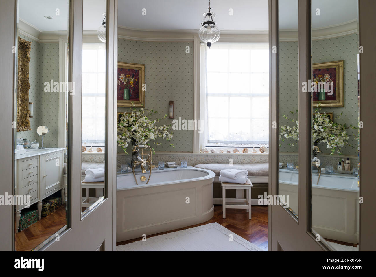 View through mirrored doors to bathroom with silk wallpaper and Italian damask blind window seat Stock Photo