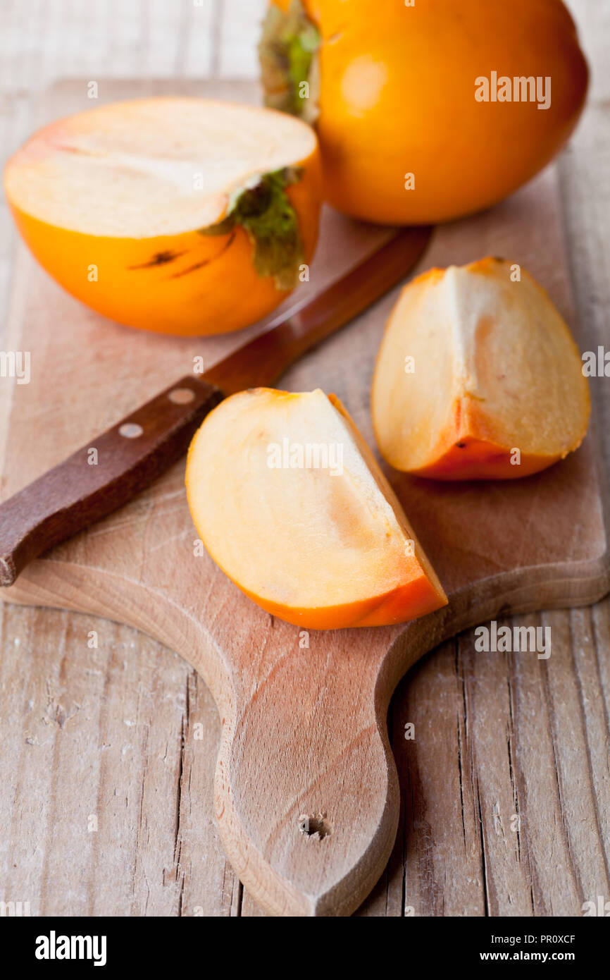 ripe persimmons and knife on wooden board Stock Photo