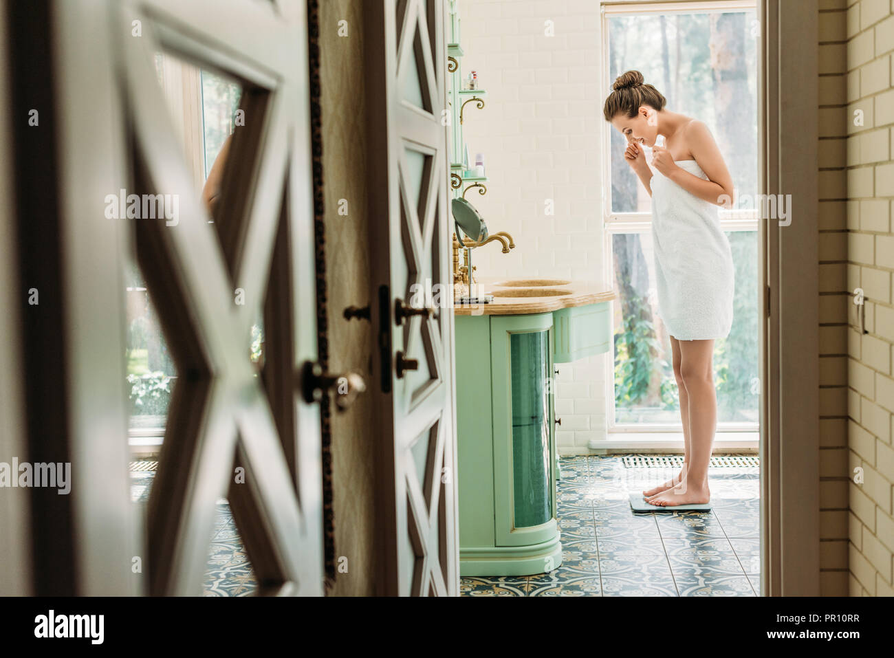 side view of young woman standing on digital scales in bathroom Stock Photo