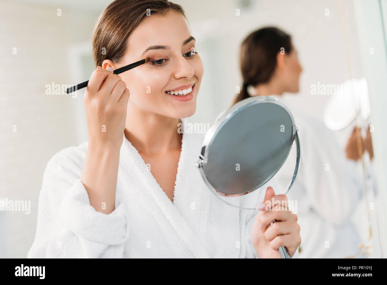 beautiful smiling girl applying makeup in bathroom Stock Photo