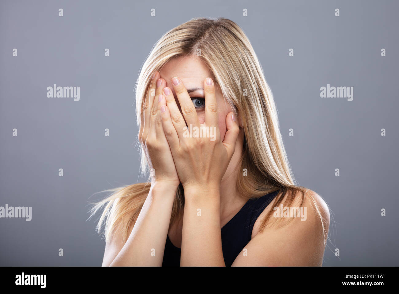 Close-up Of A Scared Woman Peeking Through Fingers Stock Photo