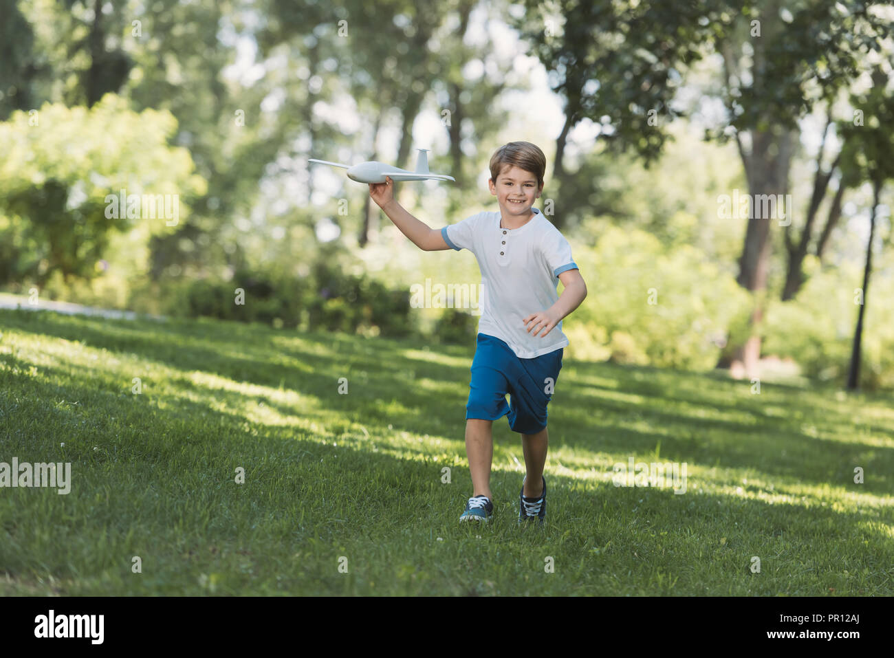 adorable happy boy holding toy plane and smiling at camera in park Stock Photo