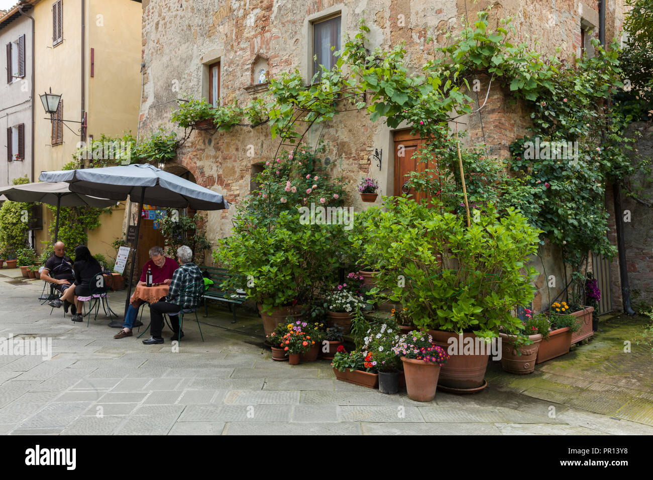 People sitting outside at a restaurant within a small courtyard surrounded by flowers in Pienza, Tuscany, Italy, Europe Stock Photo