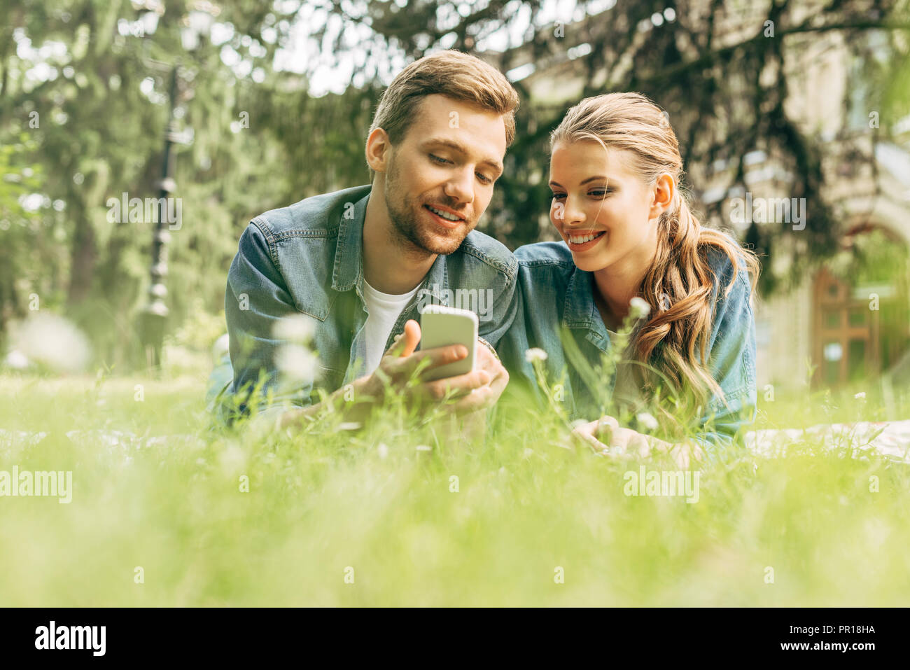 happy young couple lying on grass at park and using smartphone Stock ...