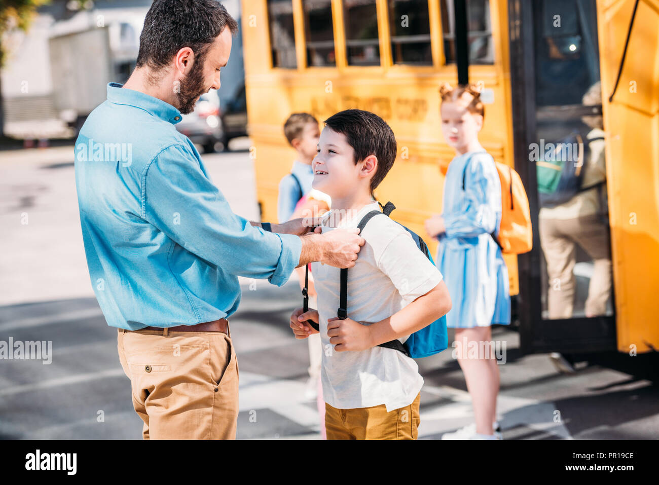 handsome father talking to his son before school in front of school bus with his classmates Stock Photo