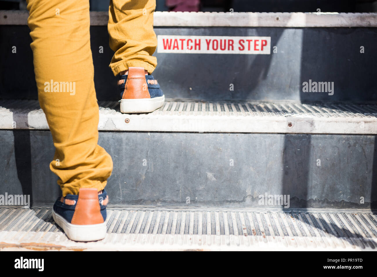 cropped shot of child going upstairs in bus with 'watch your step' sign Stock Photo