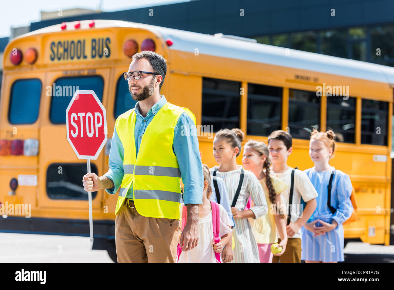 traffic guard crossing road with schoolchildren in front of school bus Stock Photo