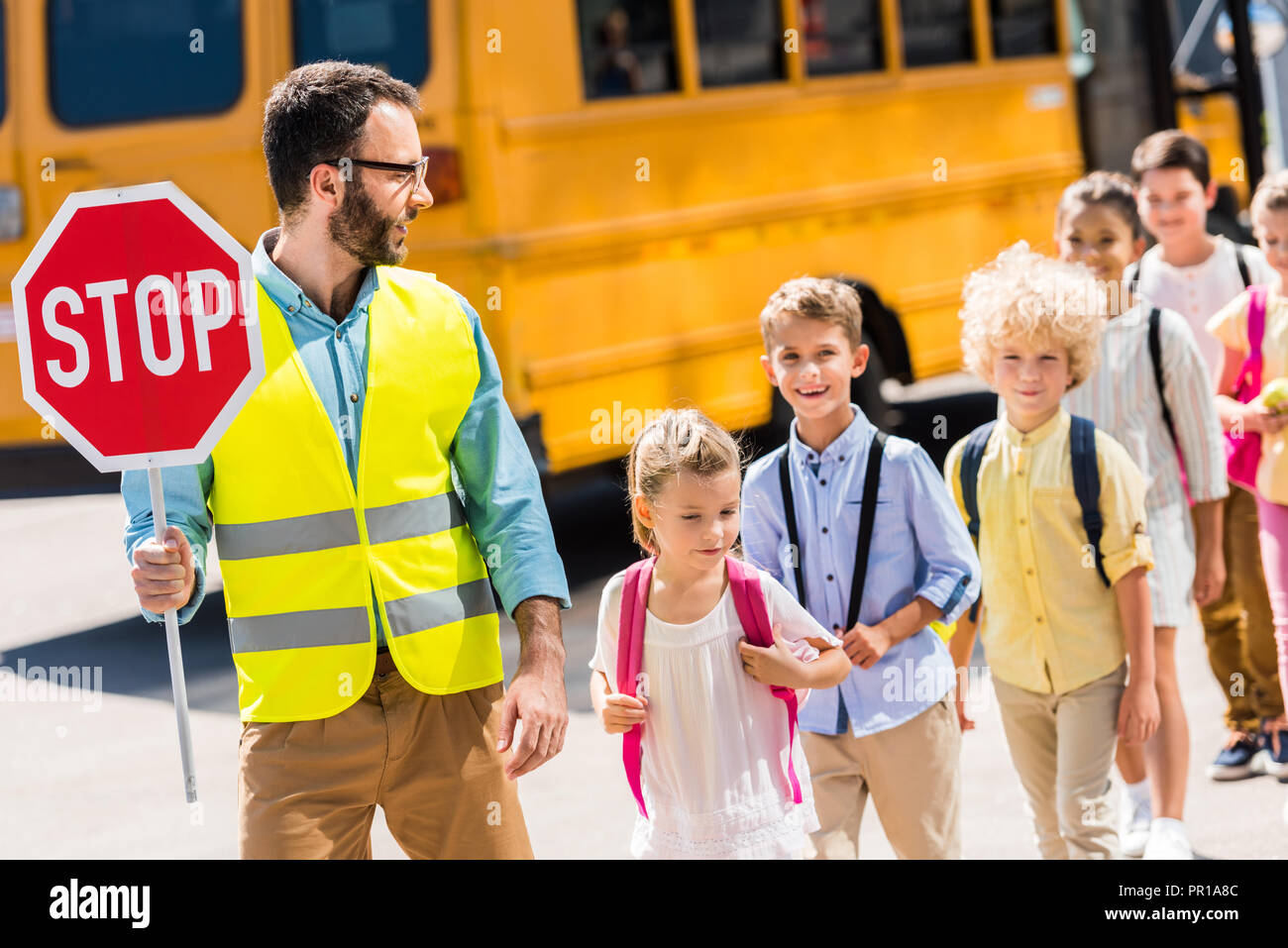 handsome traffic guard crossing road with pupils in front of school bus Stock Photo
