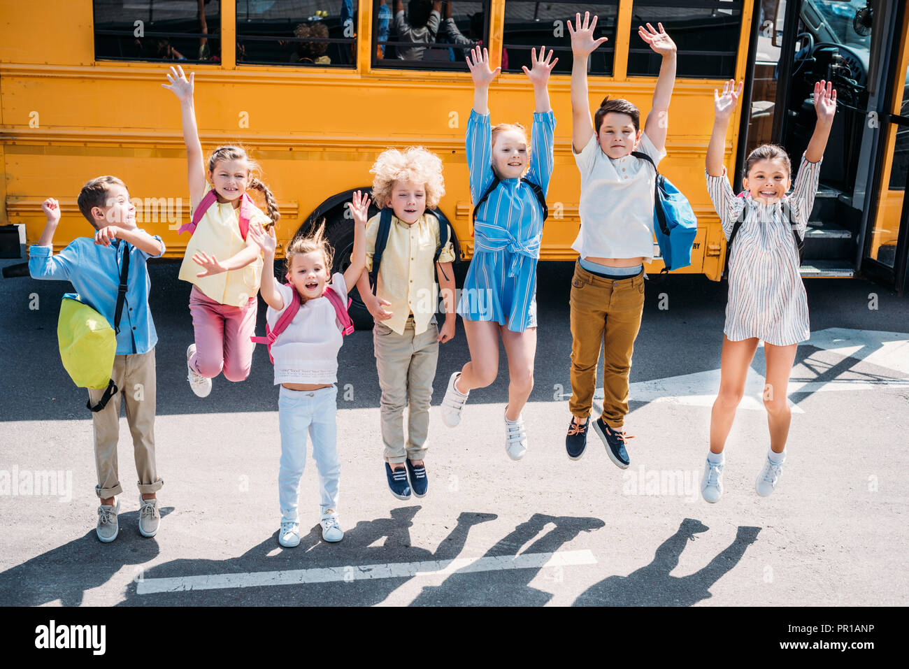 group of adorable schoolchildren jumping in front of school bus and