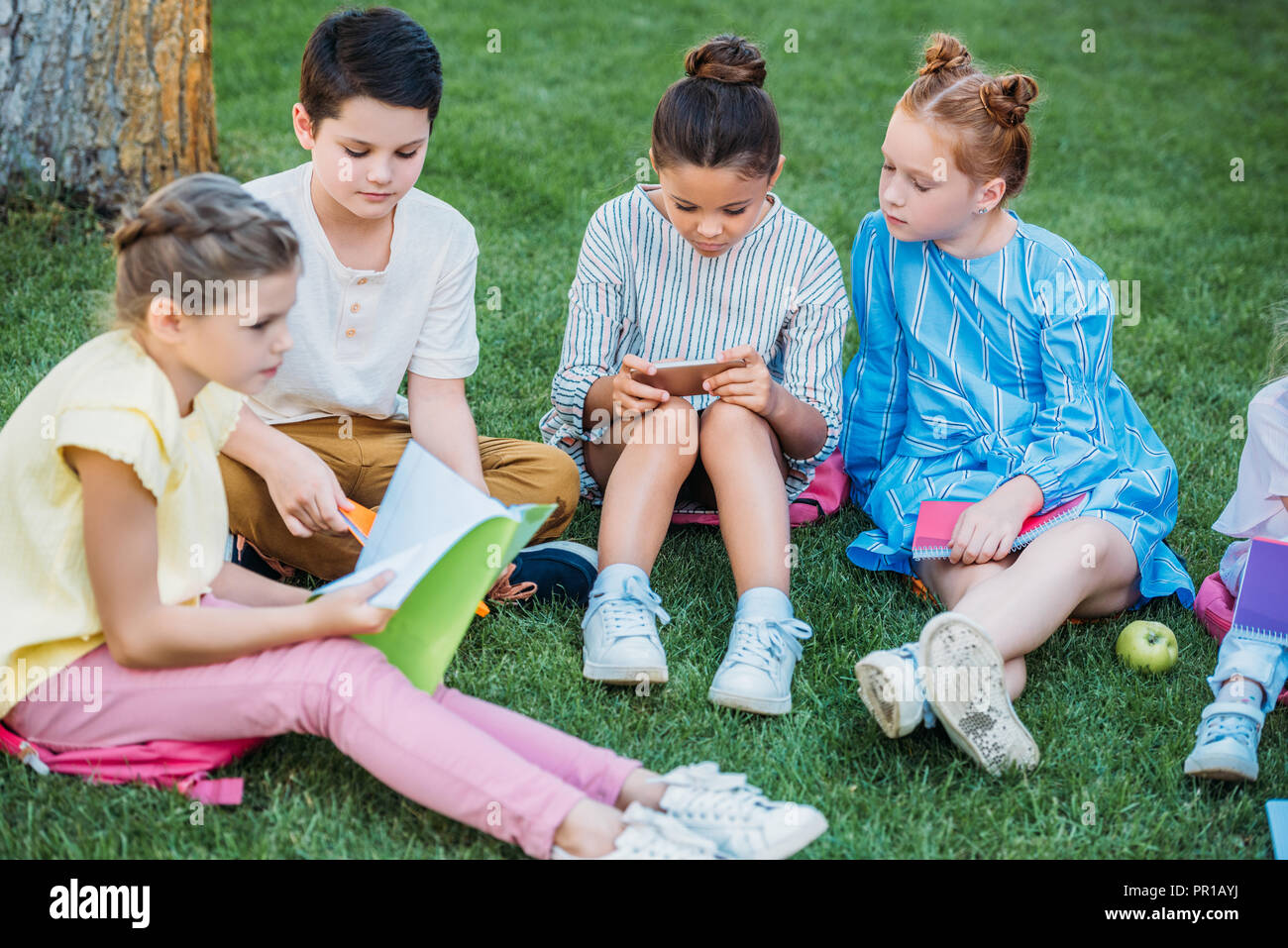 group of adorable pupils spending time together on grass after school Stock Photo
