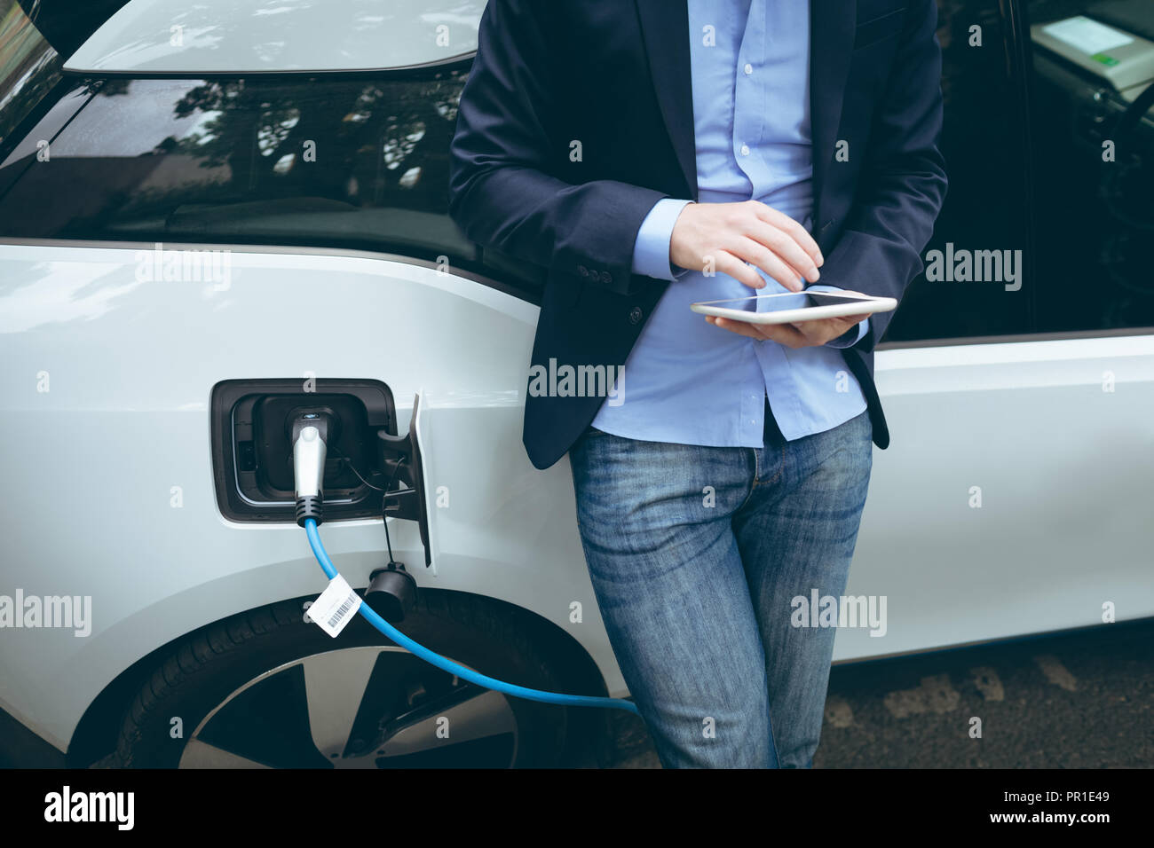 Businessman using digital tablet while charging electric car Stock Photo