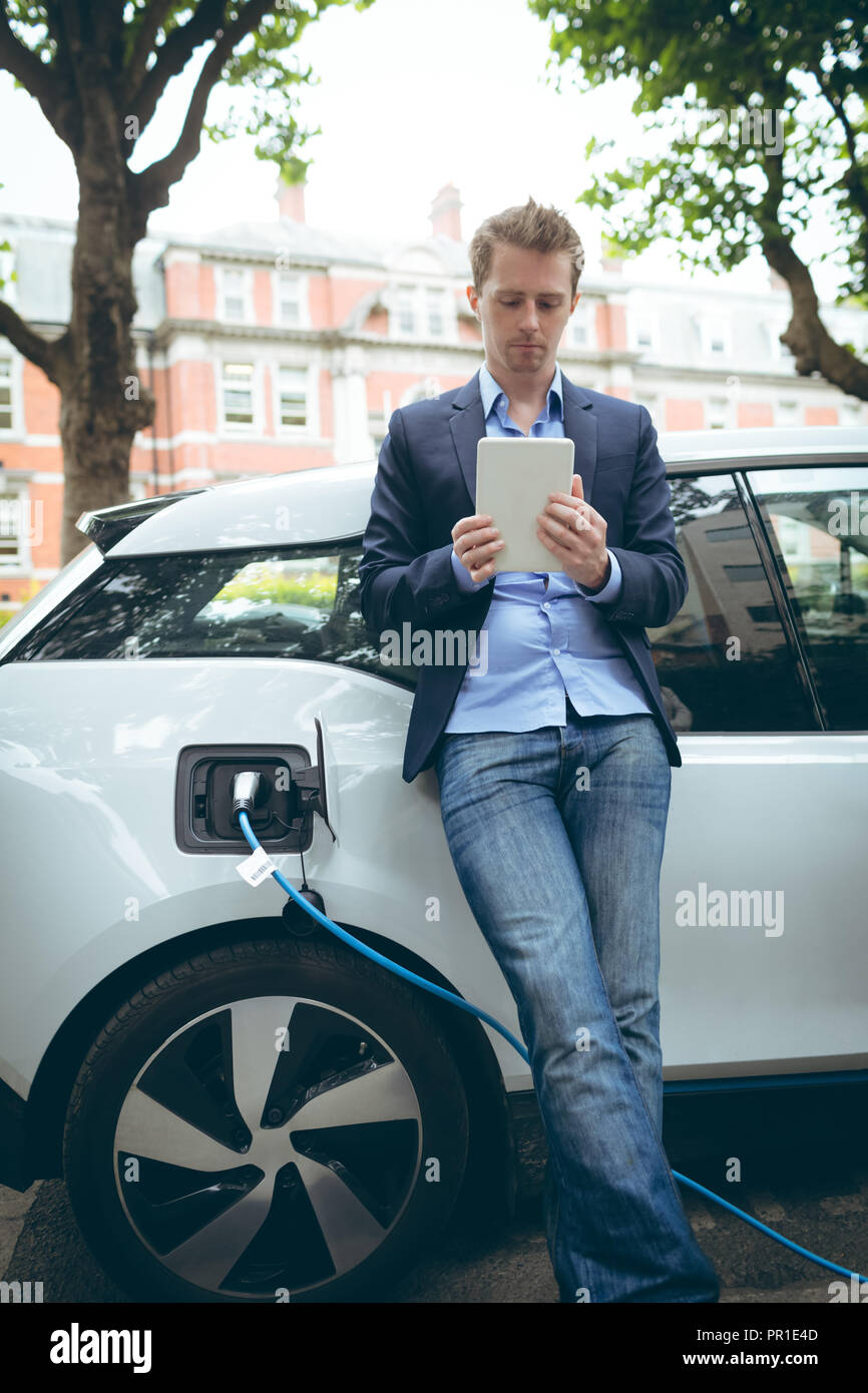 Businessman using digital tablet while charging electric car Stock Photo
