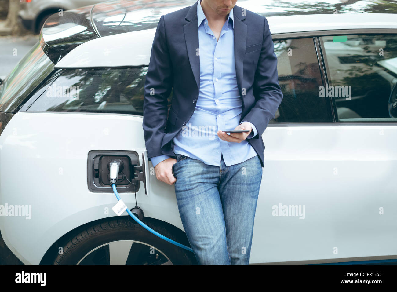 Businessman using mobile phone while charging electric car at charging station Stock Photo