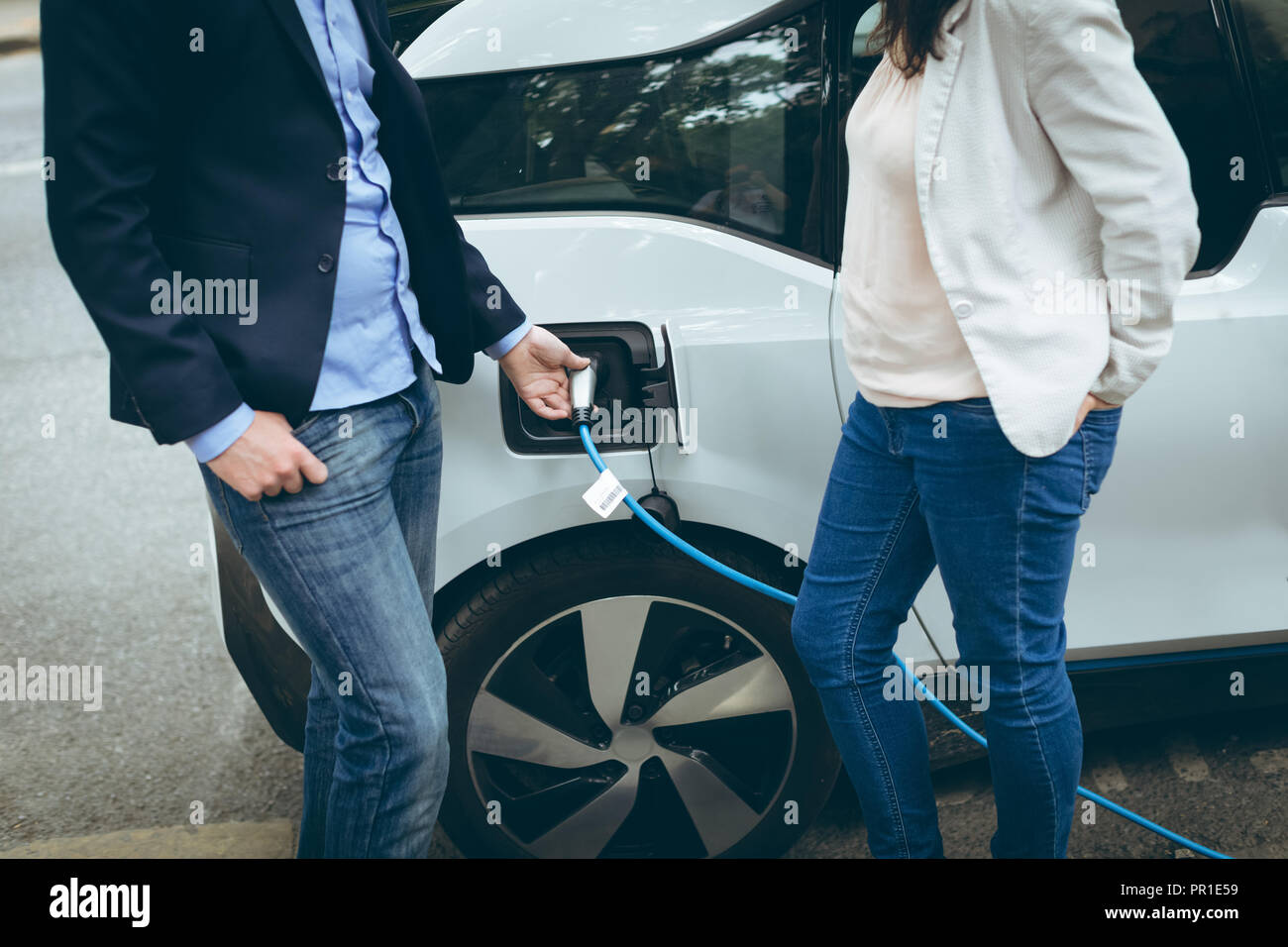 Business colleagues charging electric car at charging station Stock Photo