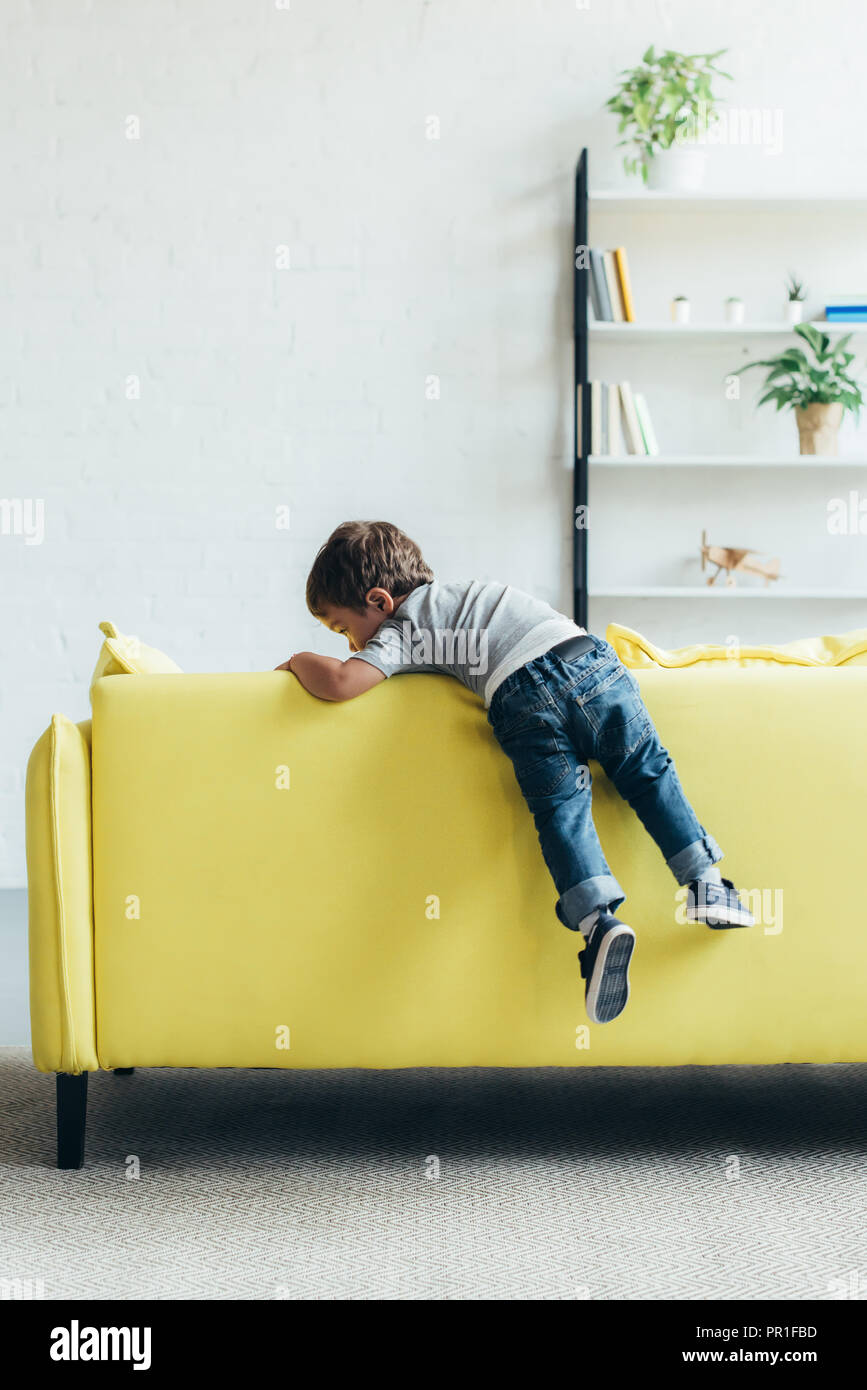 little boy climbing up on yellow sofa at home Stock Photo Alamy