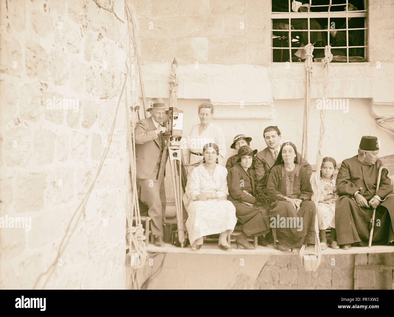Eric and Edith Matson with movie camera, standing on platform suspended from building, with other people, Jerusalem?. 1925 Stock Photo