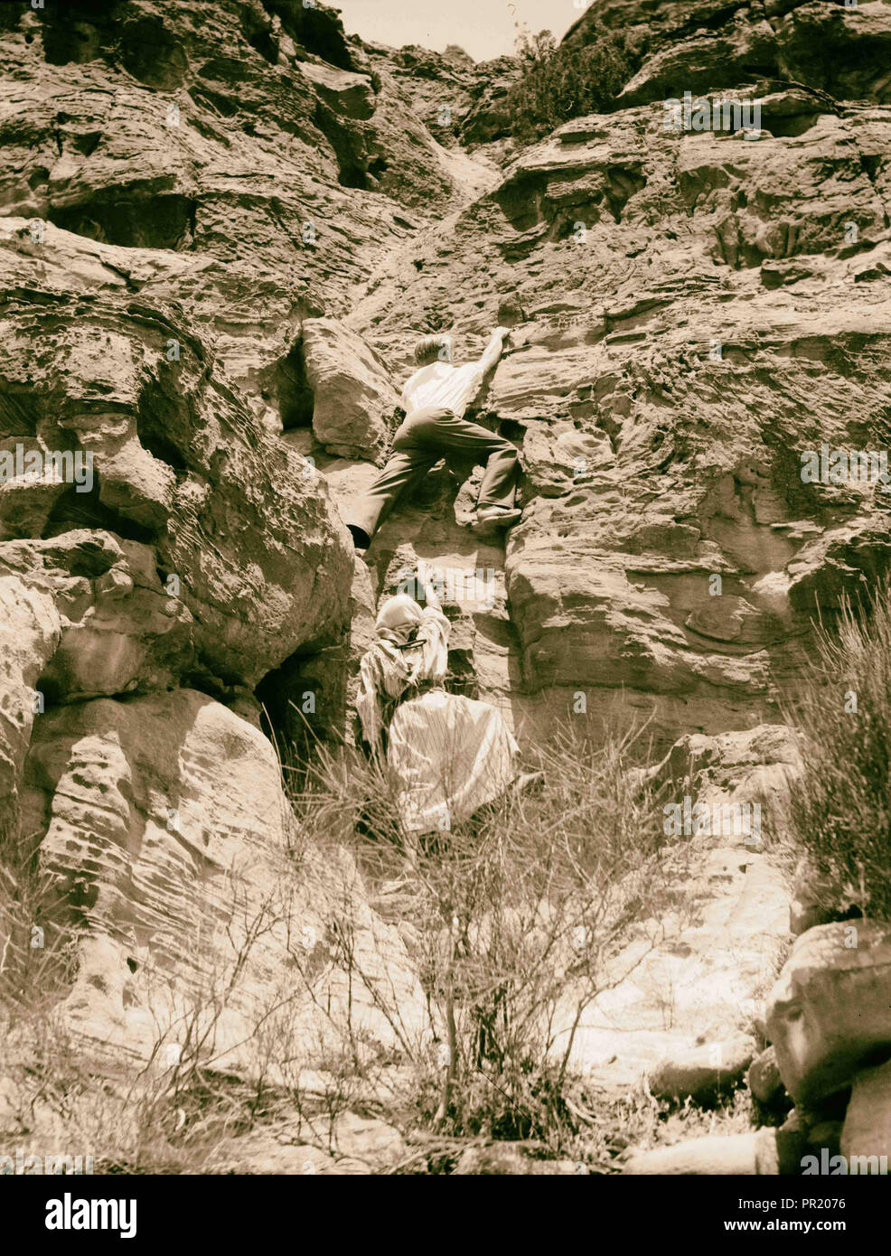 Petra. Umm el-Biyarah. (Earliest Nabatean stronghold). Final ascent showing climber scaling a difficult pass. 1920, Jordan Stock Photo