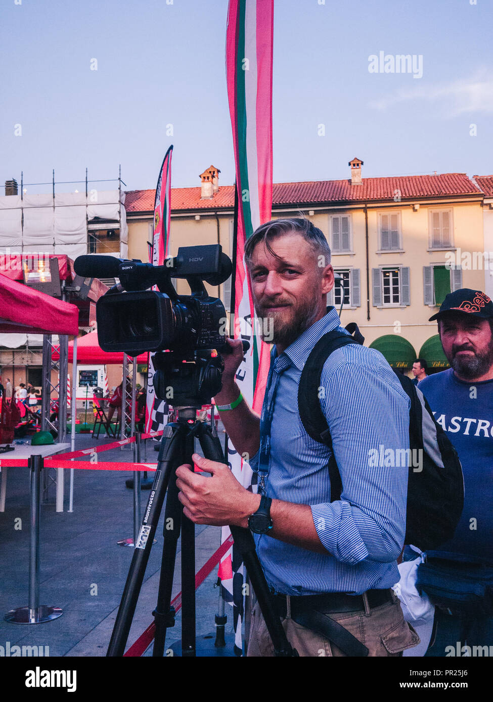 Snap of a camera man in Monza, Italy. Looks surprised. There are flags all around. Looks shocked with a nice video camera microphone and tripod Stock Photo