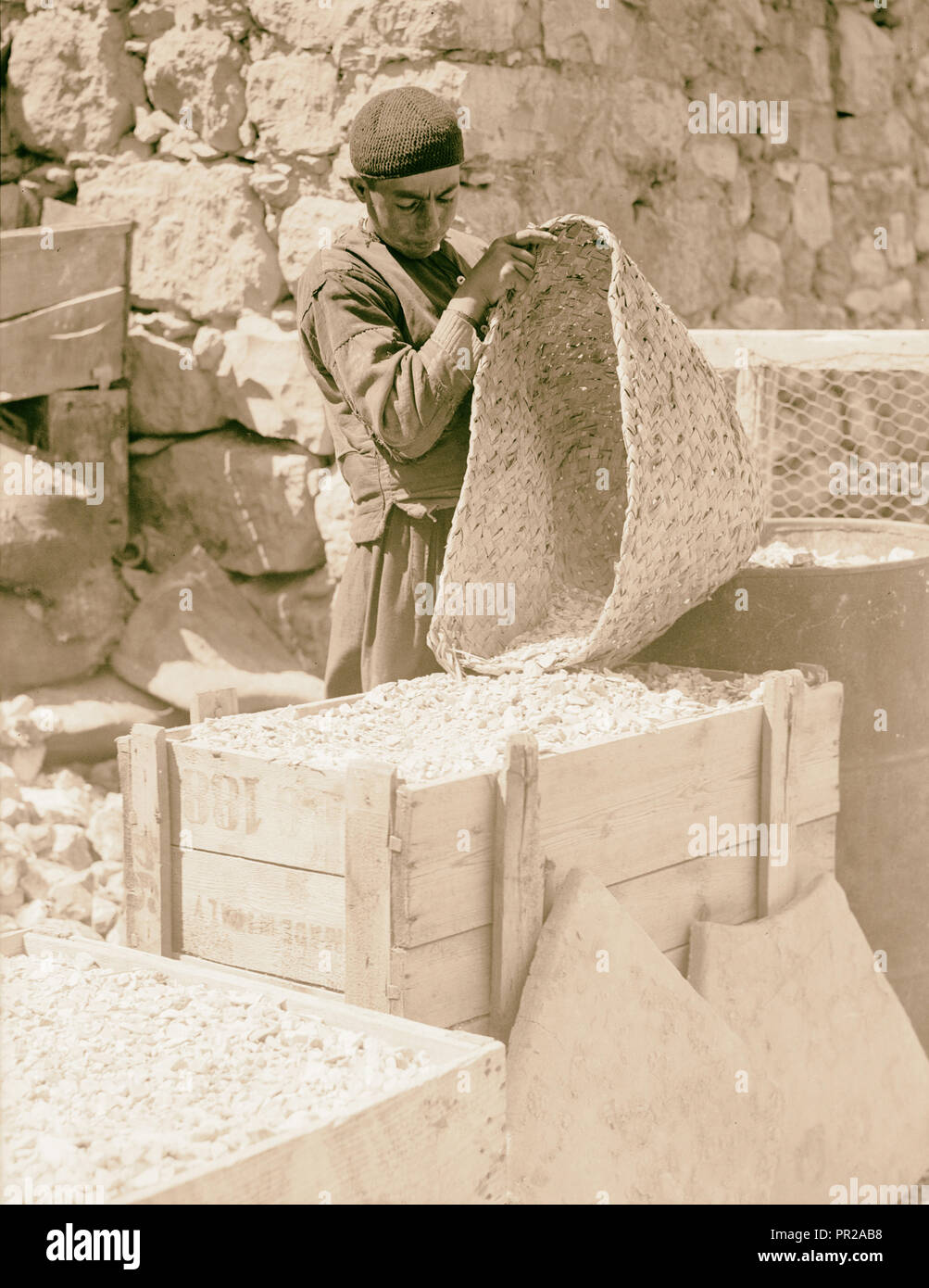 Ground flint. Photograph shows a man emptying a basket of gound flint into a wooden box. 1934, Middle East, Israel Stock Photo