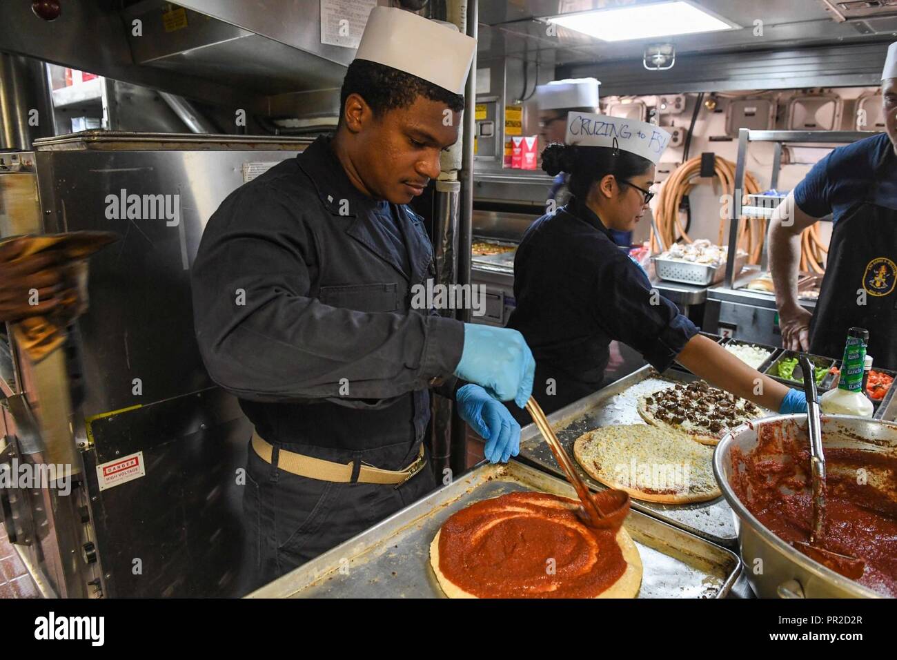 ATLANTIC OCEAN (July 22, 2017) - Lt. j.g. Reuben Carson, from Birmingham, Alabama, left, and Lt. j.g. Joanna Cruz, from Lorton, Virgina,  middle, make pizzas aboard the Arleigh Burke-class guided-missile destroyer USS James E. Williams (DDG 95) July 22, 2017. James E. Williams, home-ported in Norfolk, is on a routine deployment to the U.S. 6th Fleet area of operations in support of U.S. national security interests in Europe. Stock Photo