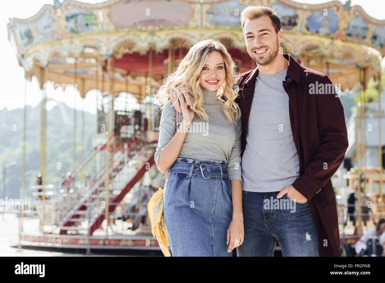smiling affectionate couple in autumn outfit cuddling near carousel in  amusement park and looking at camera Stock Photo - Alamy
