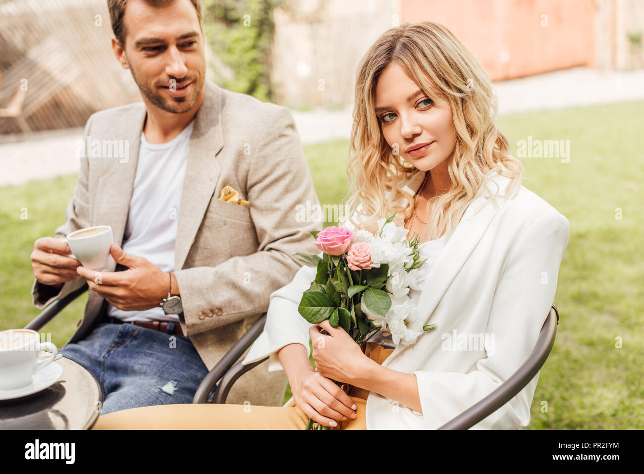 attractive girlfriend holding bouquet of flowers in cafe, boyfriend holding cup of coffee Stock Photo