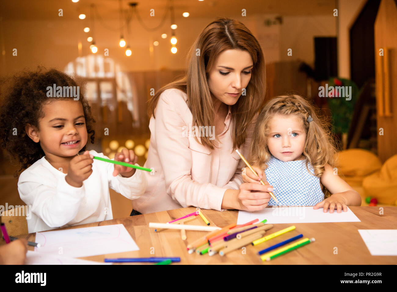 educator helping multicultural kids drawing in kindergarten Stock Photo ...