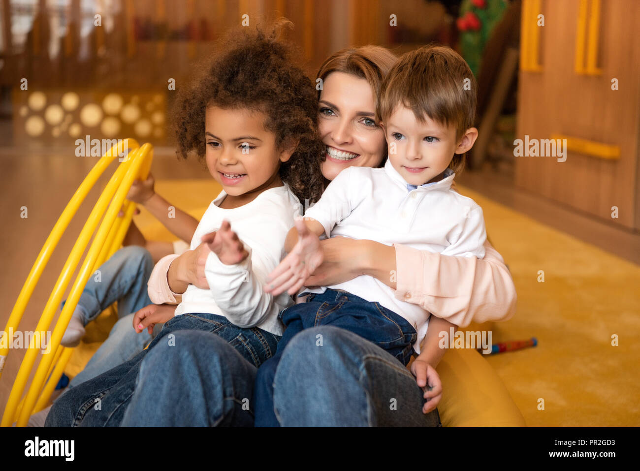 smiling educator hugging multicultural kids in kindergarten Stock Photo