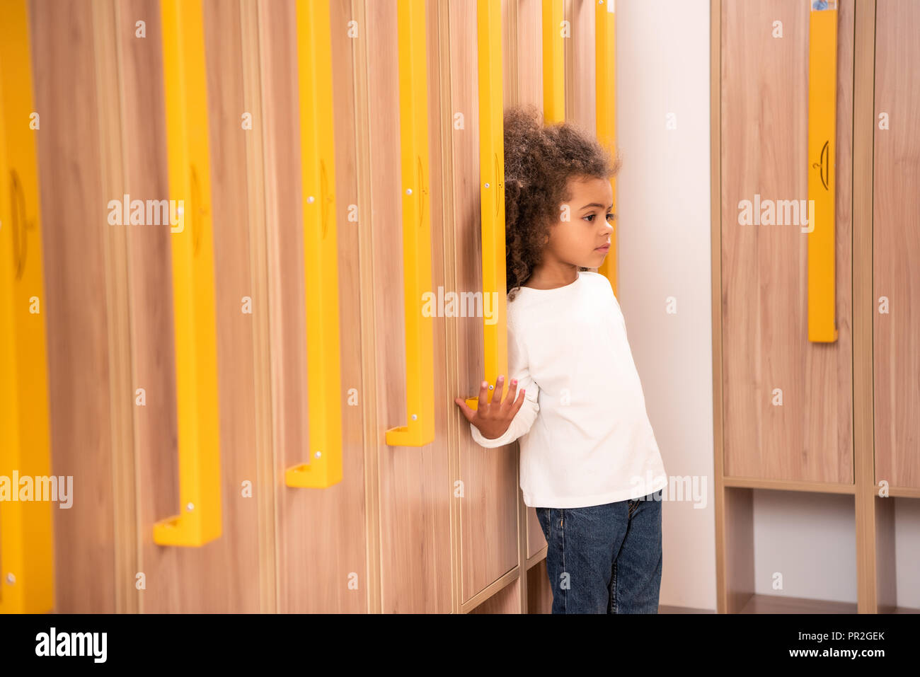 adorable african american kid standing near wooden lockers in kindergarten cloakroom Stock Photo