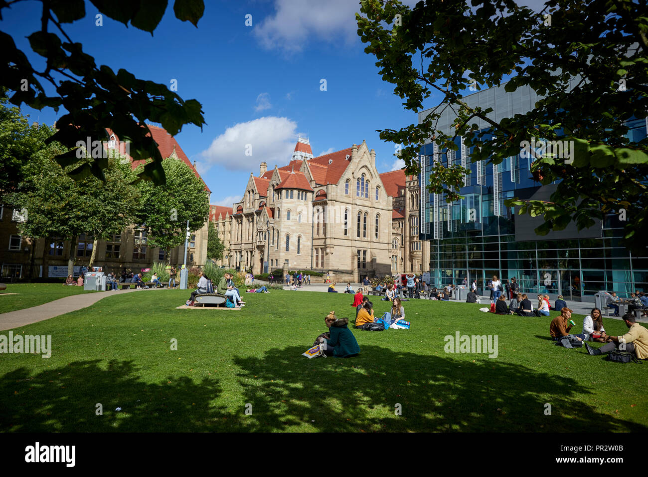 Students relaxing on the grass parks around Manchester Oxford Road Alan Gilbert Learning Commons and Whitworth Hall, Christie's Bistro net-gothic buil Stock Photo