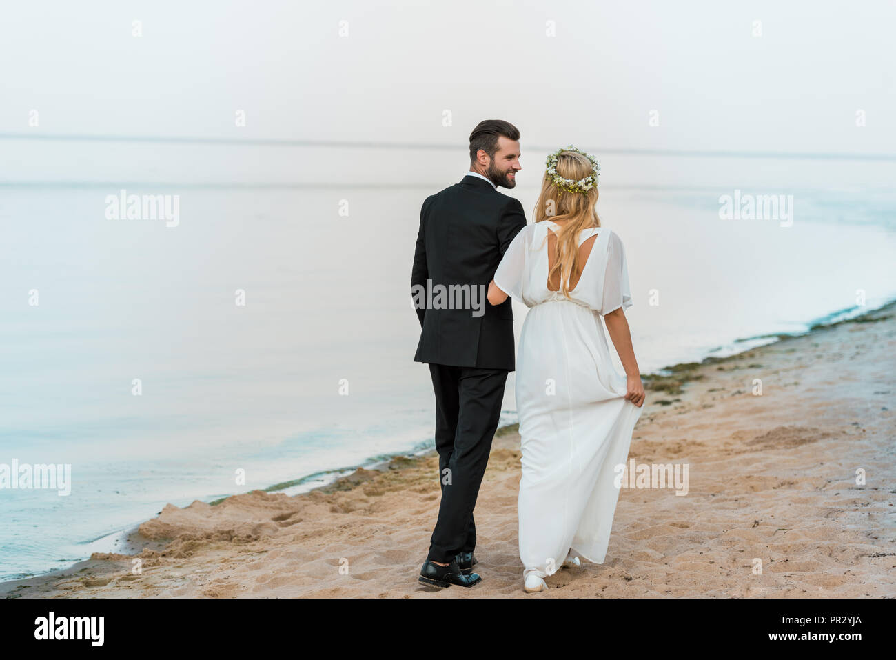 back view of wedding couple holding hands and walking on beach Stock ...