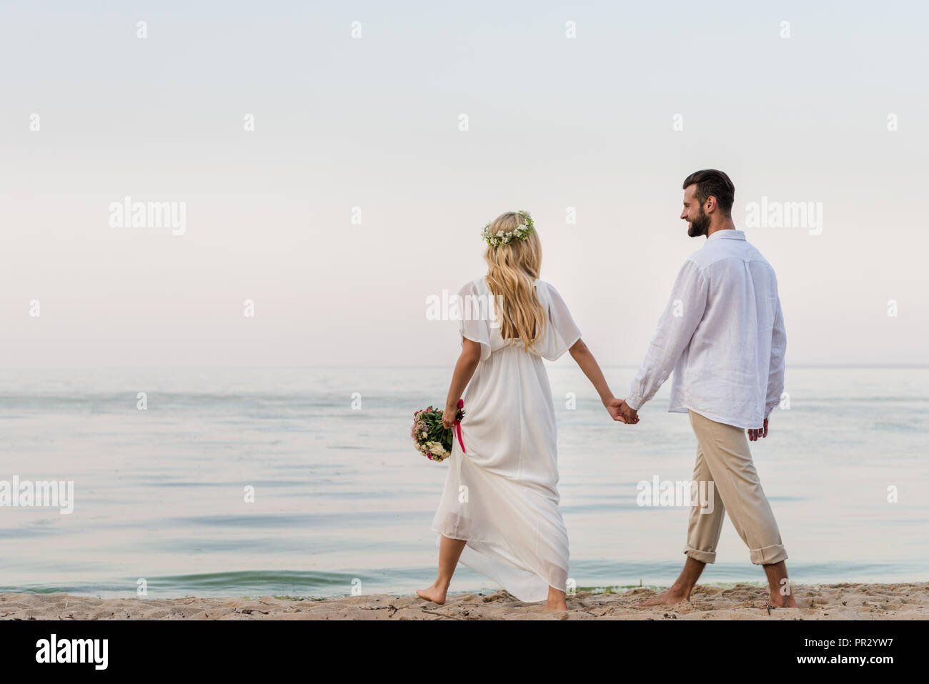 back view of bride and groom holding hands and walking with wedding ...
