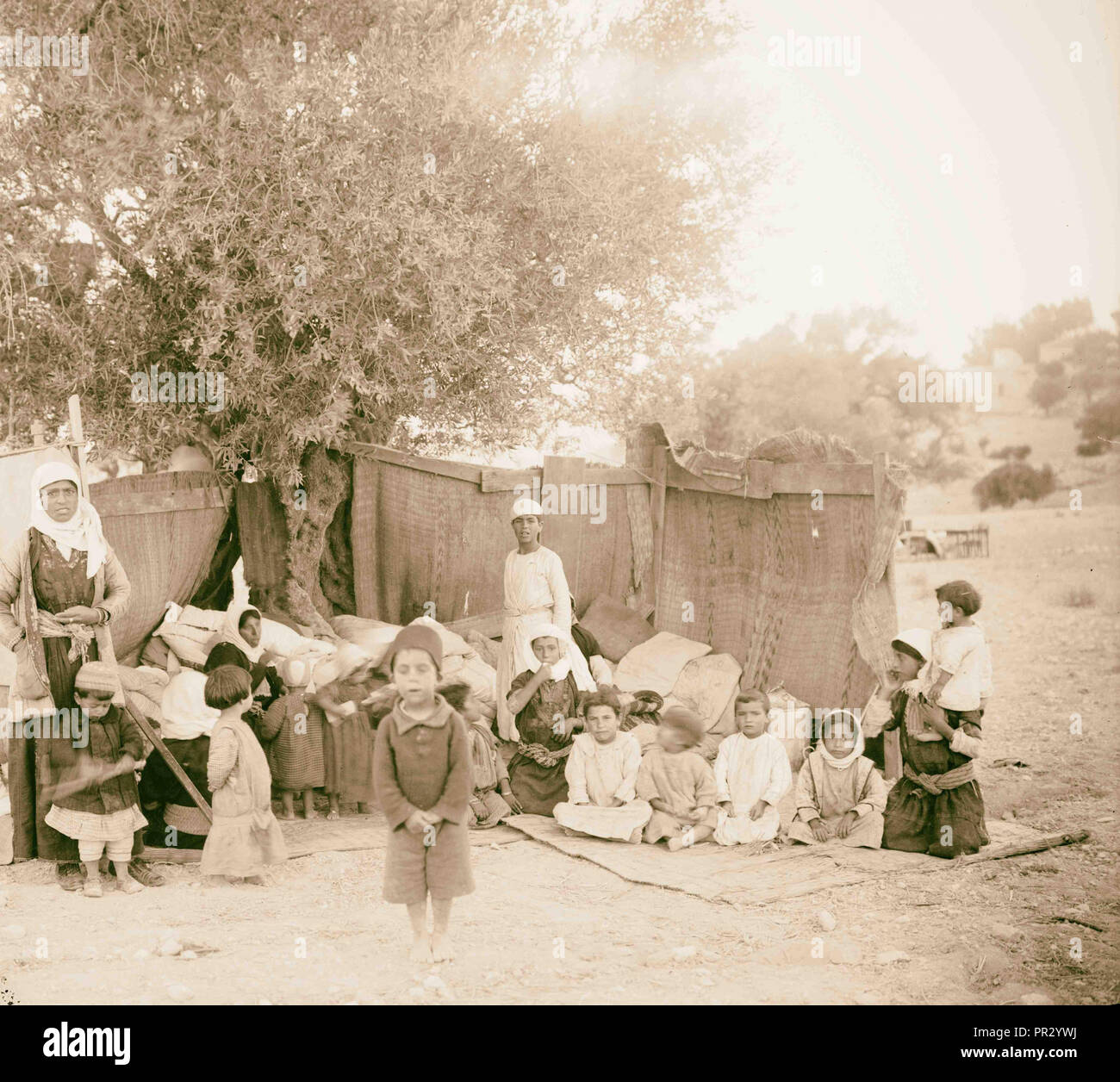 Refugees. Photograph shows women and children next to temporary shelter of woven mats underneath a tree Stock Photo