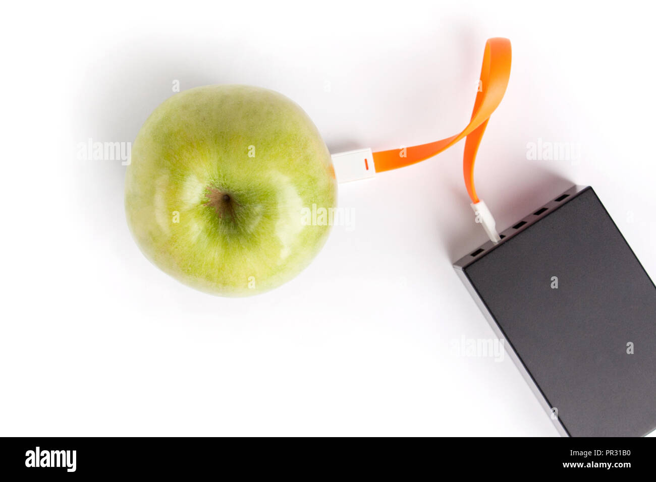 Green apple connected by an orange cable to a charger on a white isolated background Stock Photo