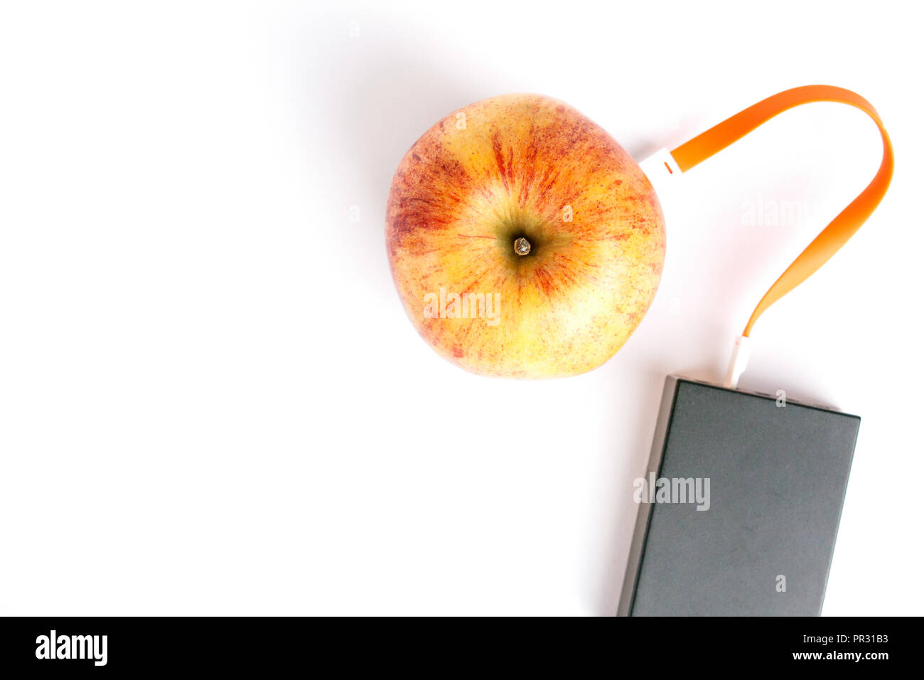 Red apple connected by an orange cable to a charger on a white isolated background. With copy space Stock Photo