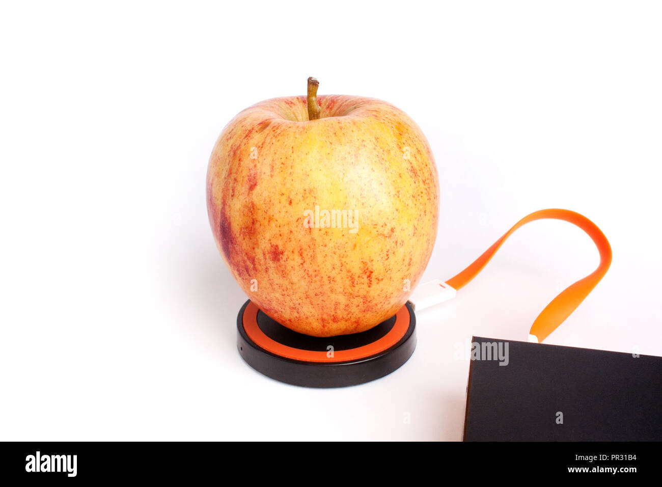 Red apple is on the platform for wireless charging by connecting an orange wire to the charger Stock Photo
