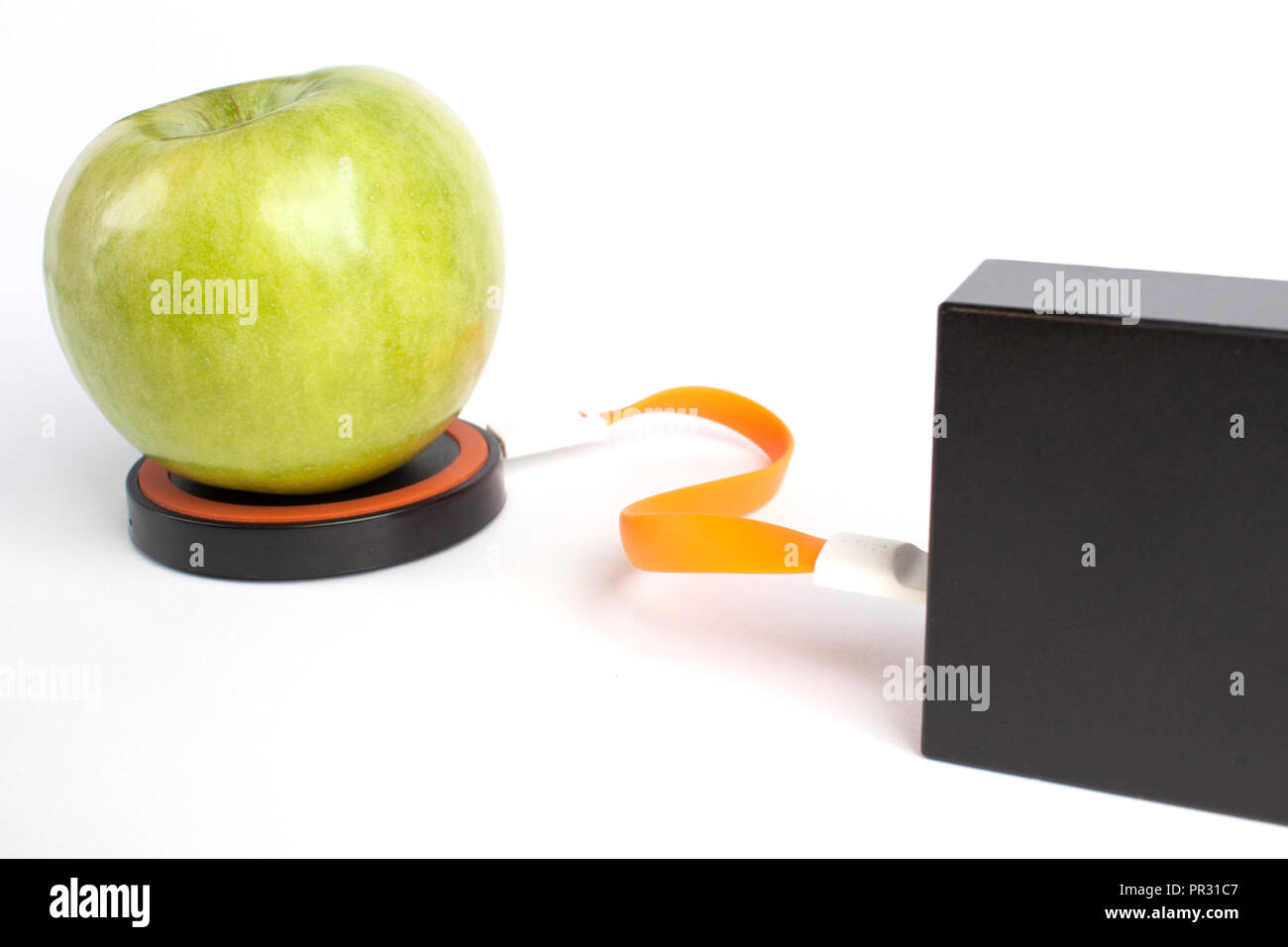 Green apple is on the platform for wireless charging by connecting an orange wire to the charger Stock Photo
