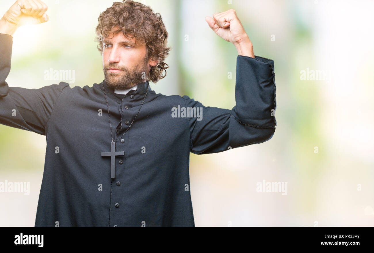 Handsome hispanic catholic priest man over isolated background showing arms muscles smiling proud. Fitness concept. Stock Photo