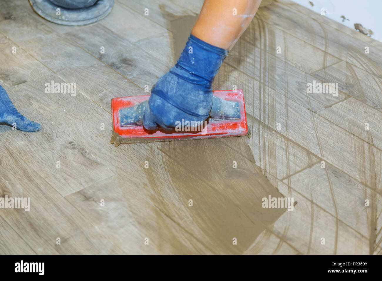 Hand of flooring on gray color of new grout tile on tile gray for the final step for flooring smoothing tile joints with a sponge Stock Photo