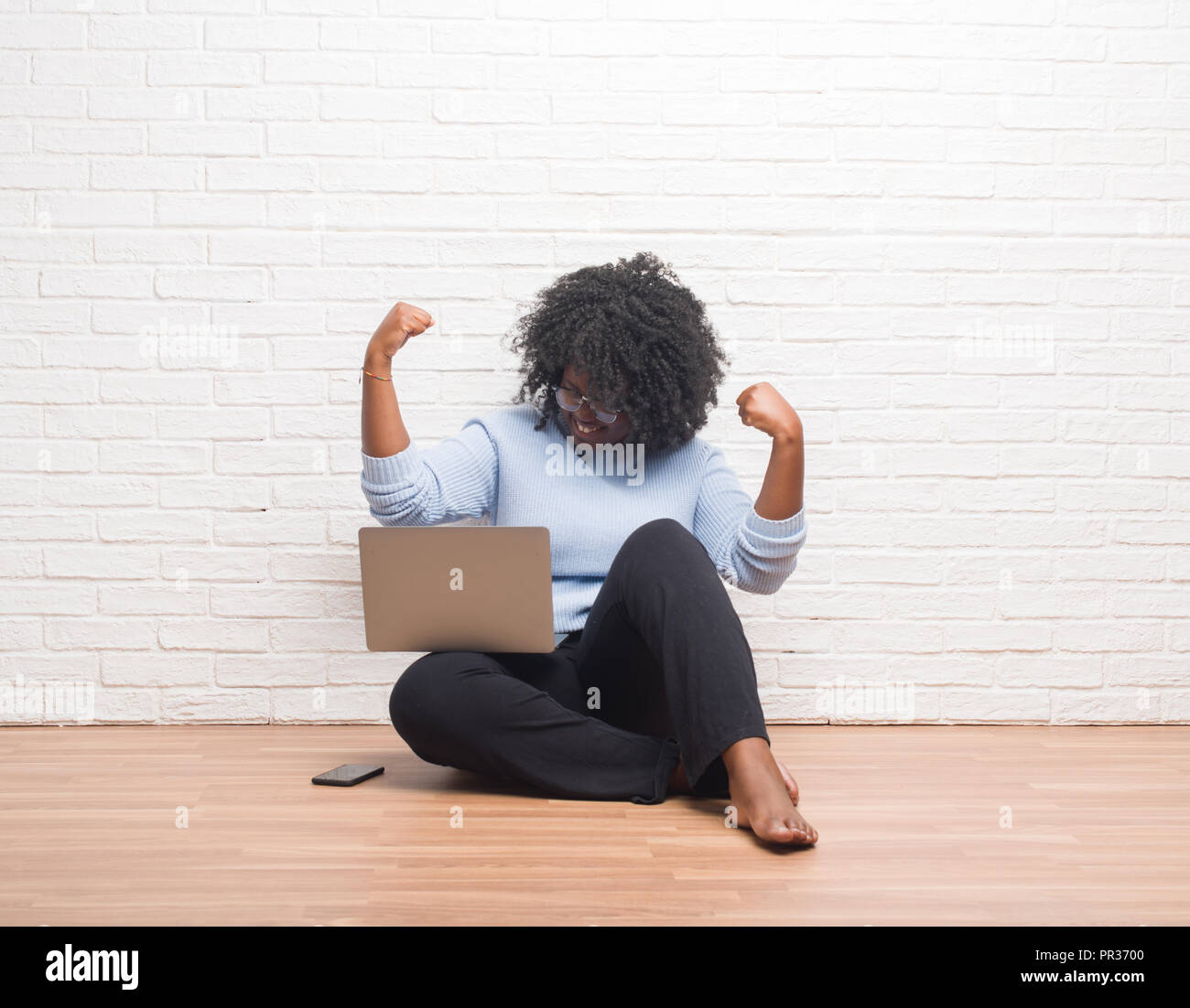 Young african american woman sitting on the floor using laptop at home ...