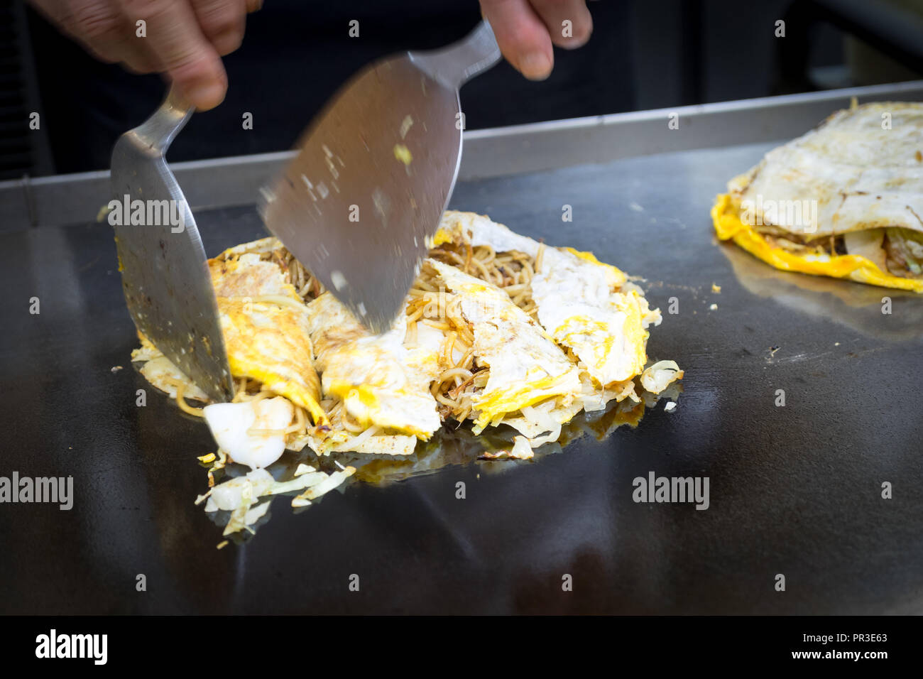 A chef makes Hiroshima style okonomiyaki at Okonomimura in Hiroshima, Japan. Stock Photo