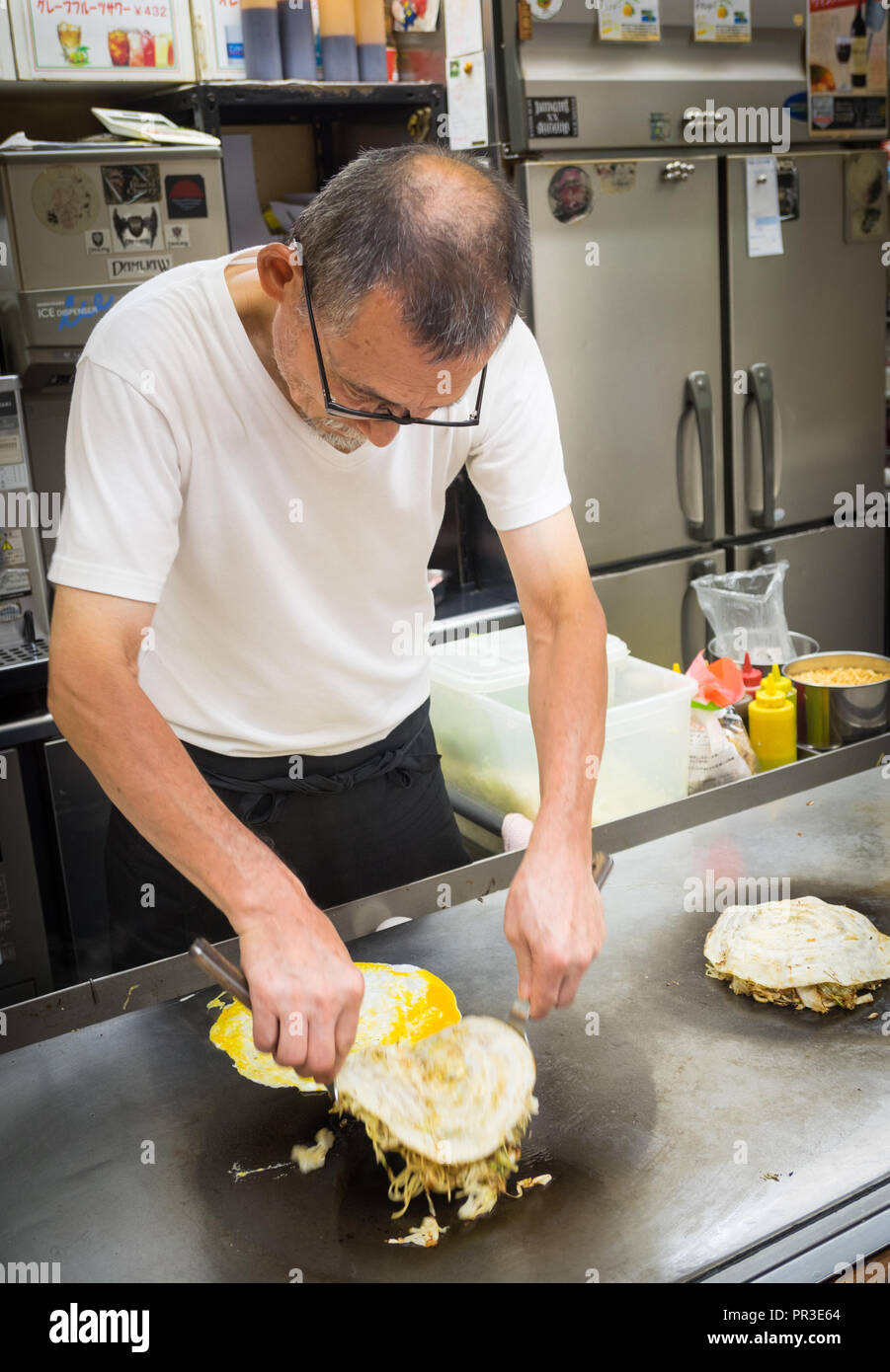 A chef makes Hiroshima style okonomiyaki at Okonomimura in Hiroshima, Japan. Stock Photo