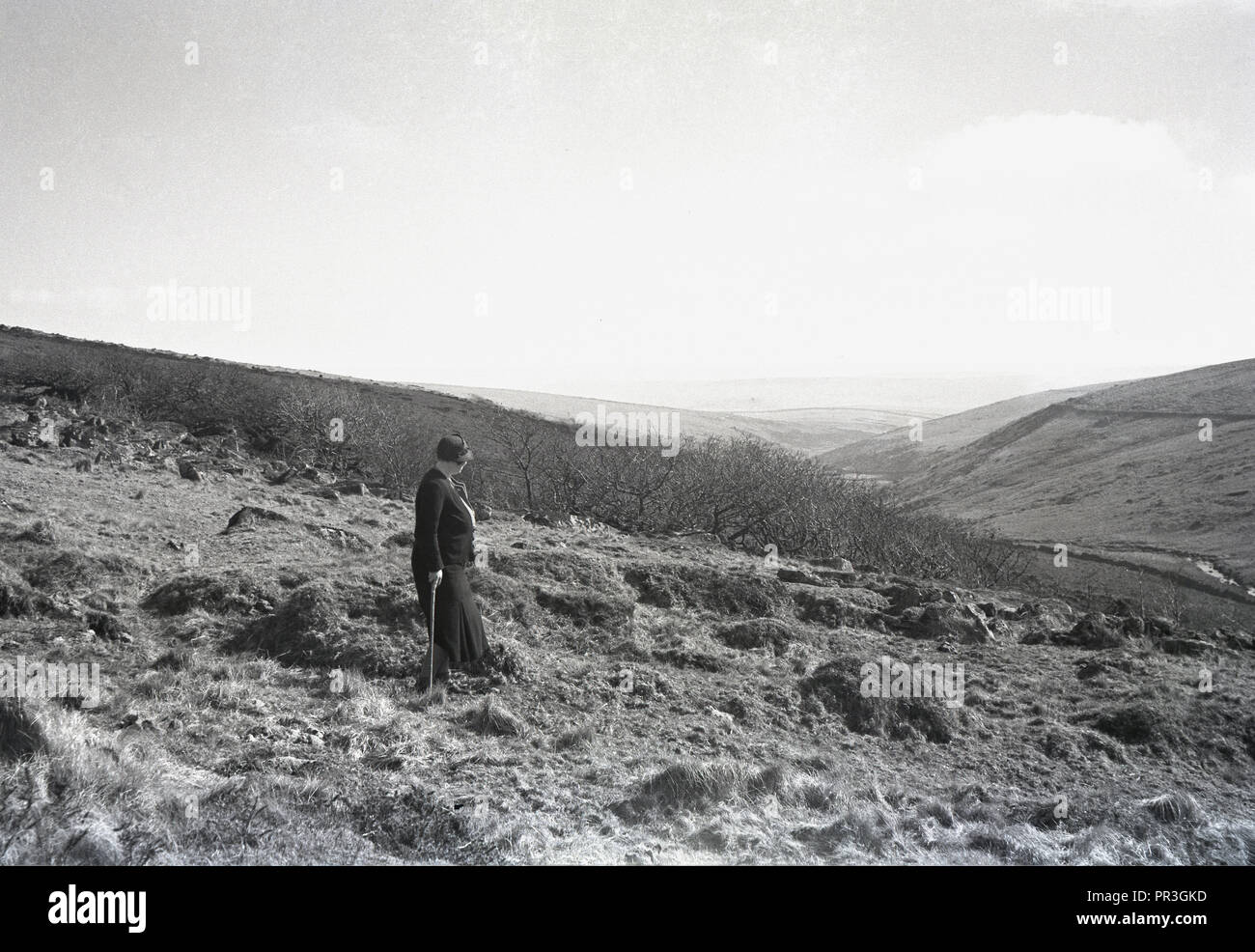 1930s, historical, a lady walker with stick standing near Longaford Tor at Dartmoor national park in Devon, England, UK, a wild natural moorland that contains many rock formations known as tors. Stock Photo