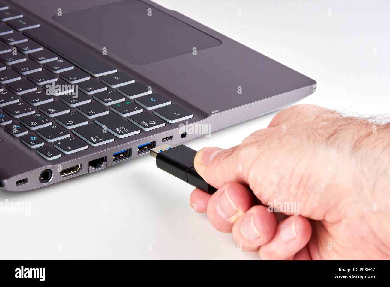 Hand of a man plugging a black USB Flash drive into a silver laptop port with a black keyboard. On a white background. Stock Photo