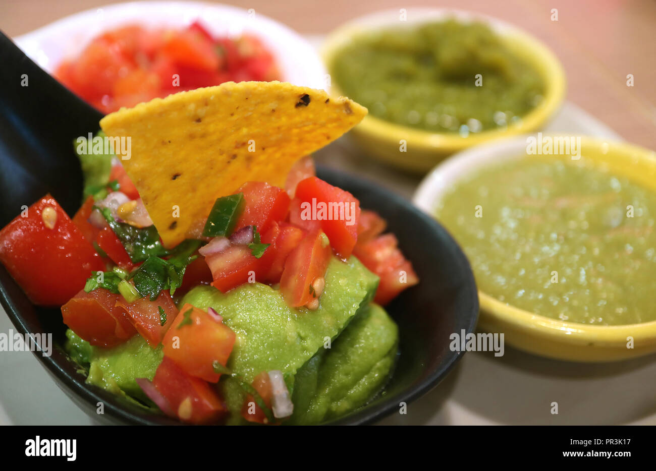 Closed Up Guacamole with Nachos Chip and Blurred Colorful Spicy Mexican Salsa Sauce in Background Stock Photo