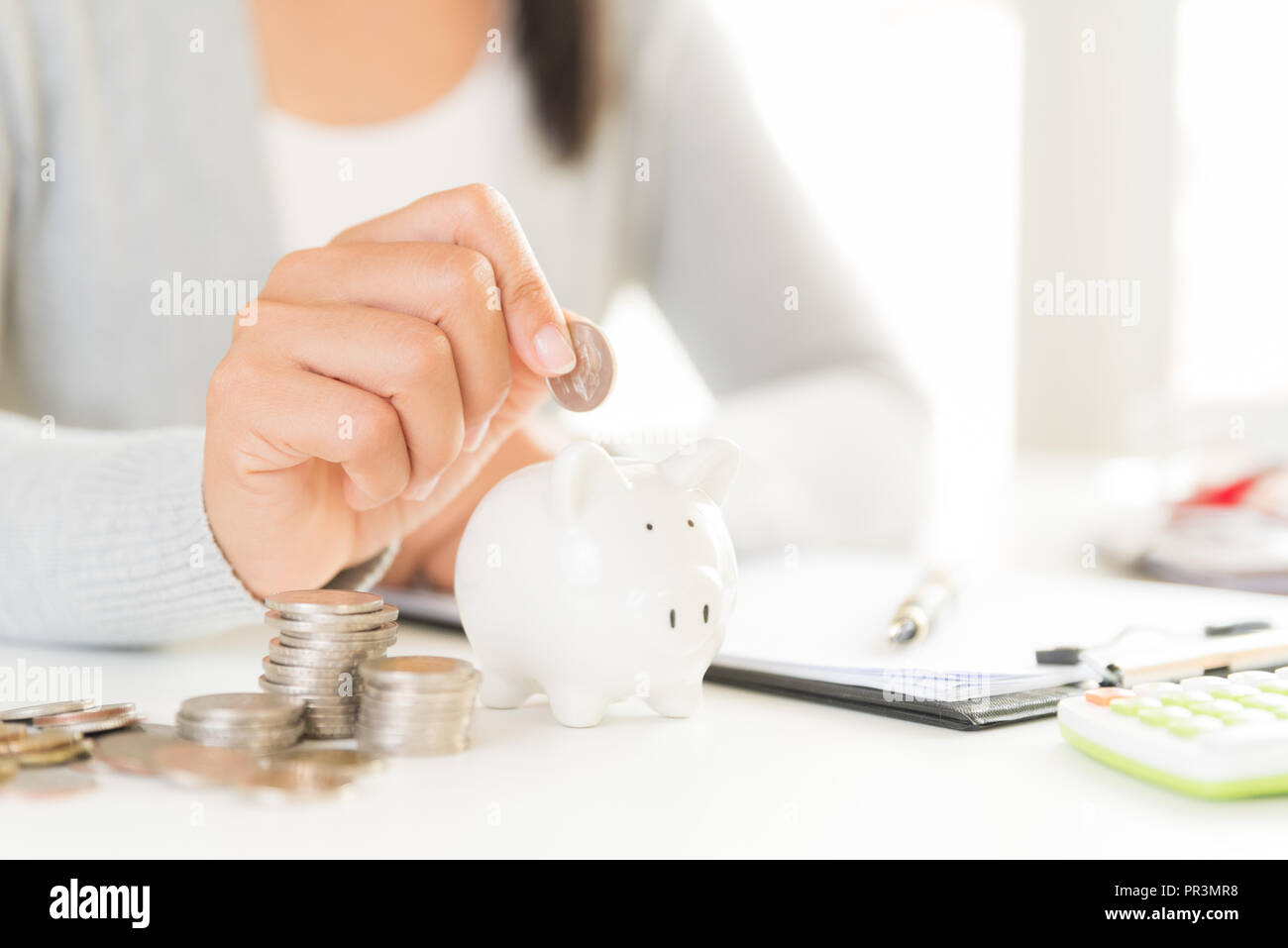 Woman hand putting money coin into piggy bank with stack of coins ...