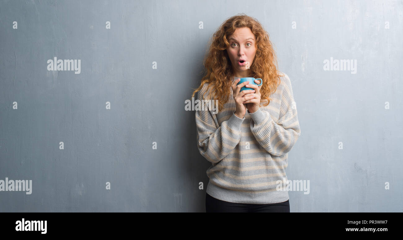 Young redhead woman over grey grunge wall drinking a cup of coffee ...
