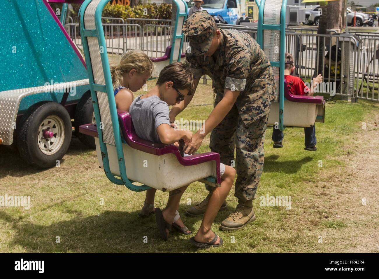 Lance Cpl. Christopher Reyes, a finance technician with Headquarters Battalion, helps children with their seatbelts on a fair ride during the Klipper Summer Bash at the Klipper Golf Course aboard Marine Corps Base Hawaii, July 28, 2017. The Summer Bash is an annual event hosted by the Klipper Golf Course to strengthen a sense of community amongst residents of MCB Hawaii. Stock Photo