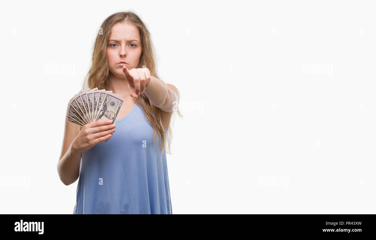Young blonde woman holding dollars pointing with finger to the camera and to you, hand sign, positive and confident gesture from the front Stock Photo